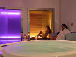 A spa room with a large hot tub, a massage table, and a wooden panel wall.