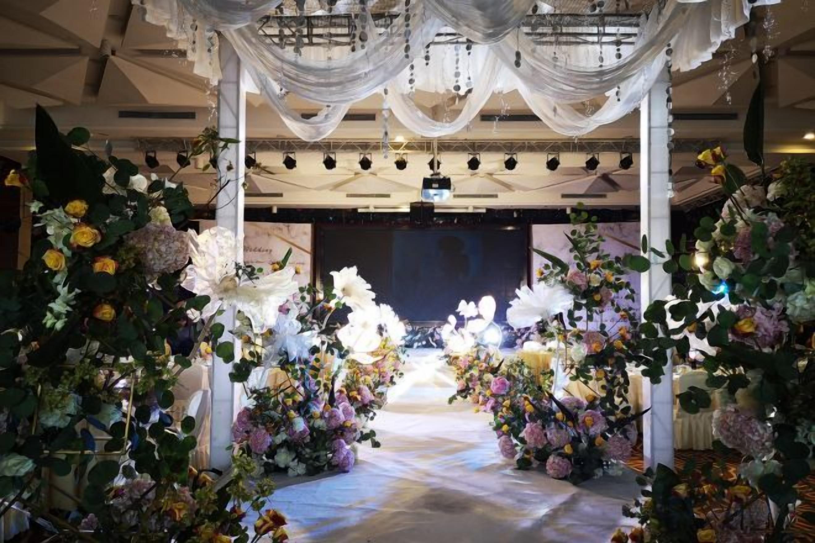 Un espace intérieur doté d’une scène, de compositions florales et de tentures décoratives suspendues au plafond.