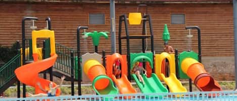 A swimming pool with multiple slides and a wooden fence in the background.