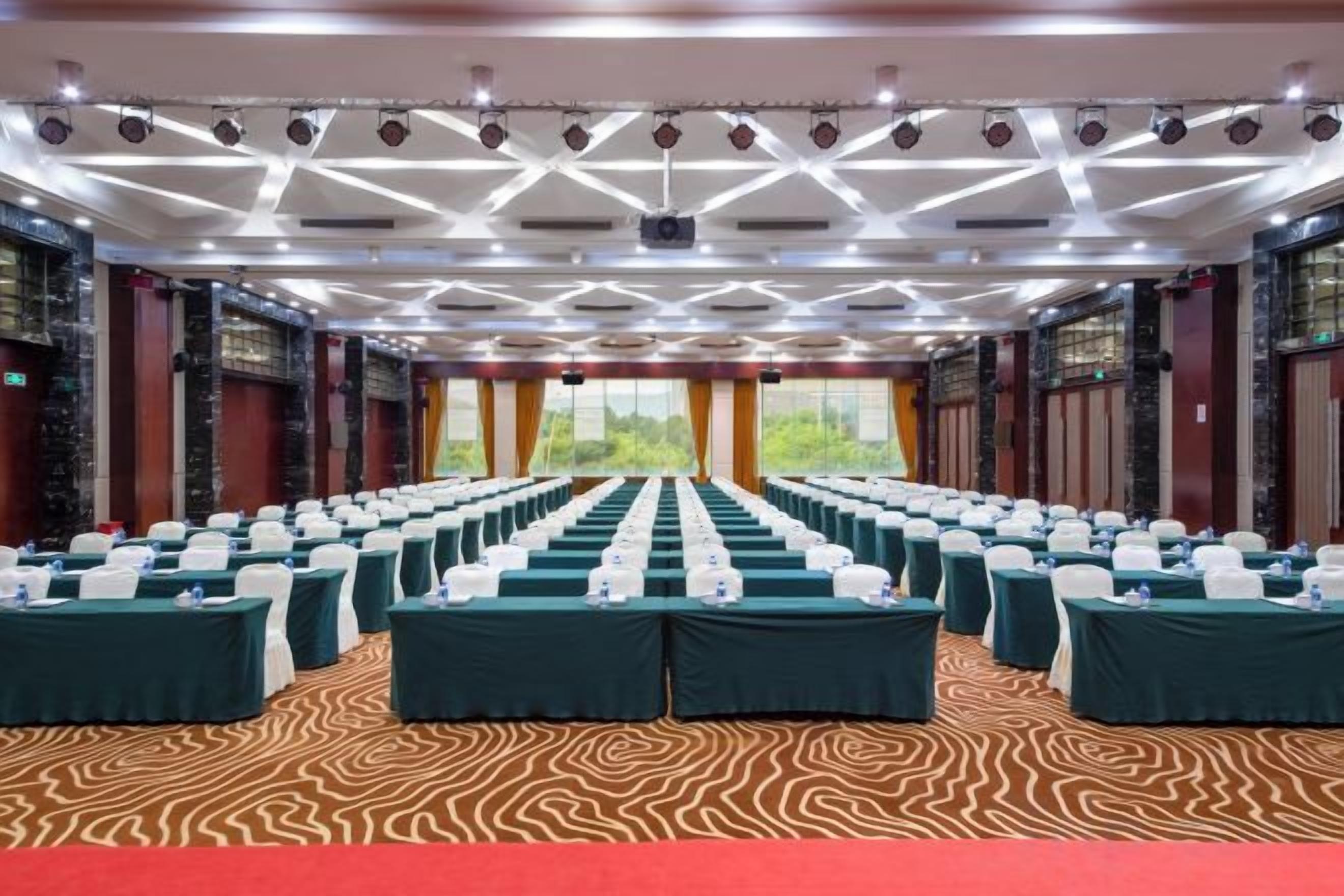 A conference room with rows of tables, chairs, and a red carpet.
