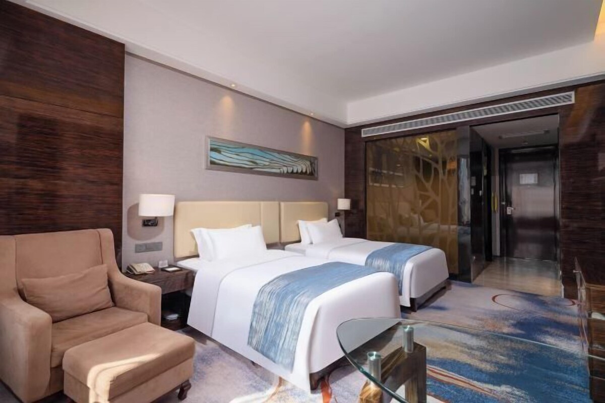 Ein Hotelzimmer mit zwei Betten, einem Sofa, einem Glastisch und einem Gemälde an der Wand.