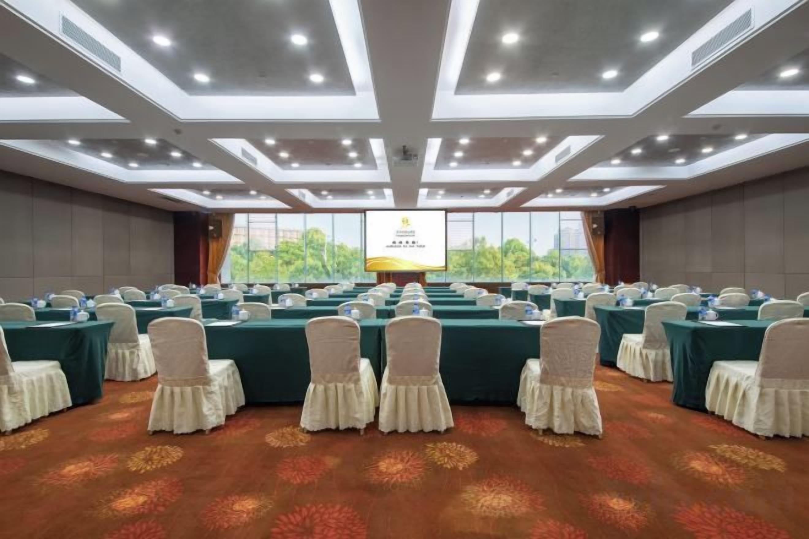 A conference room with rows of tables, chairs, and a large screen at the front.