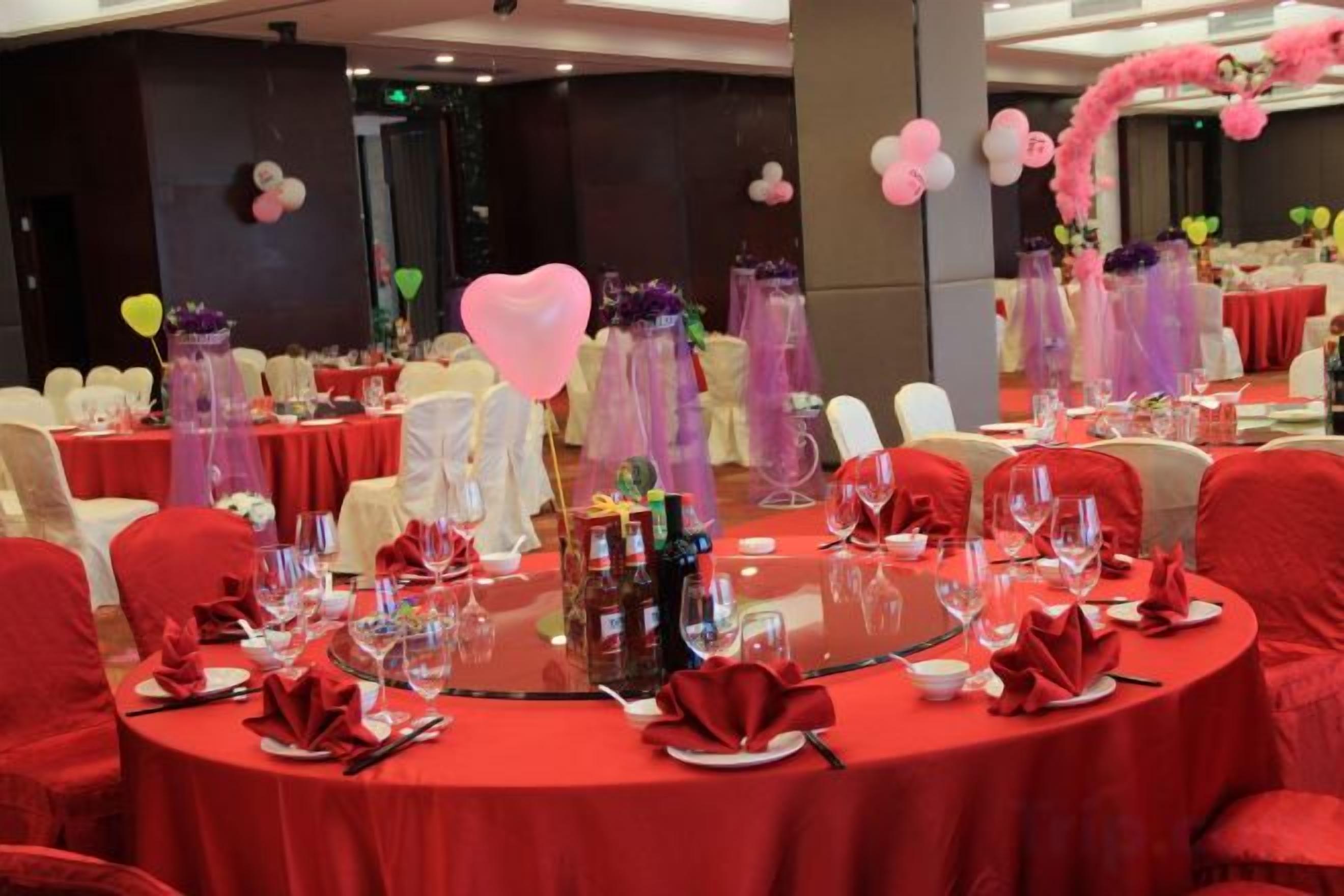 A banquet hall with round tables, red tablecloths, and white chairs.