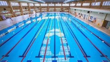 A large indoor swimming pool with multiple lanes, surrounded by windows and equipped with starting blocks.