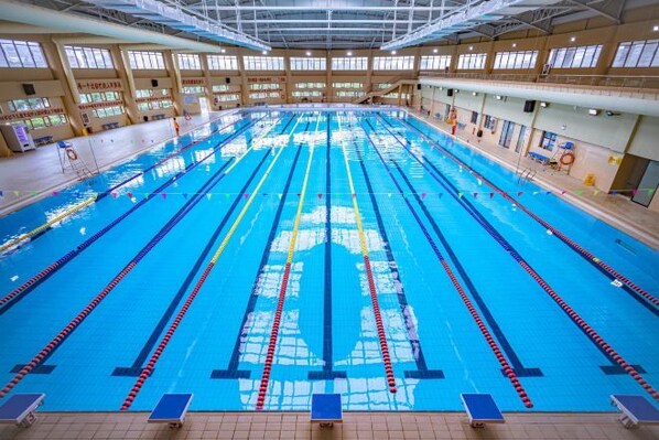 Une grande piscine intérieure dotée de plusieurs couloirs, entourée de fenêtres et équipée de plots de départ.