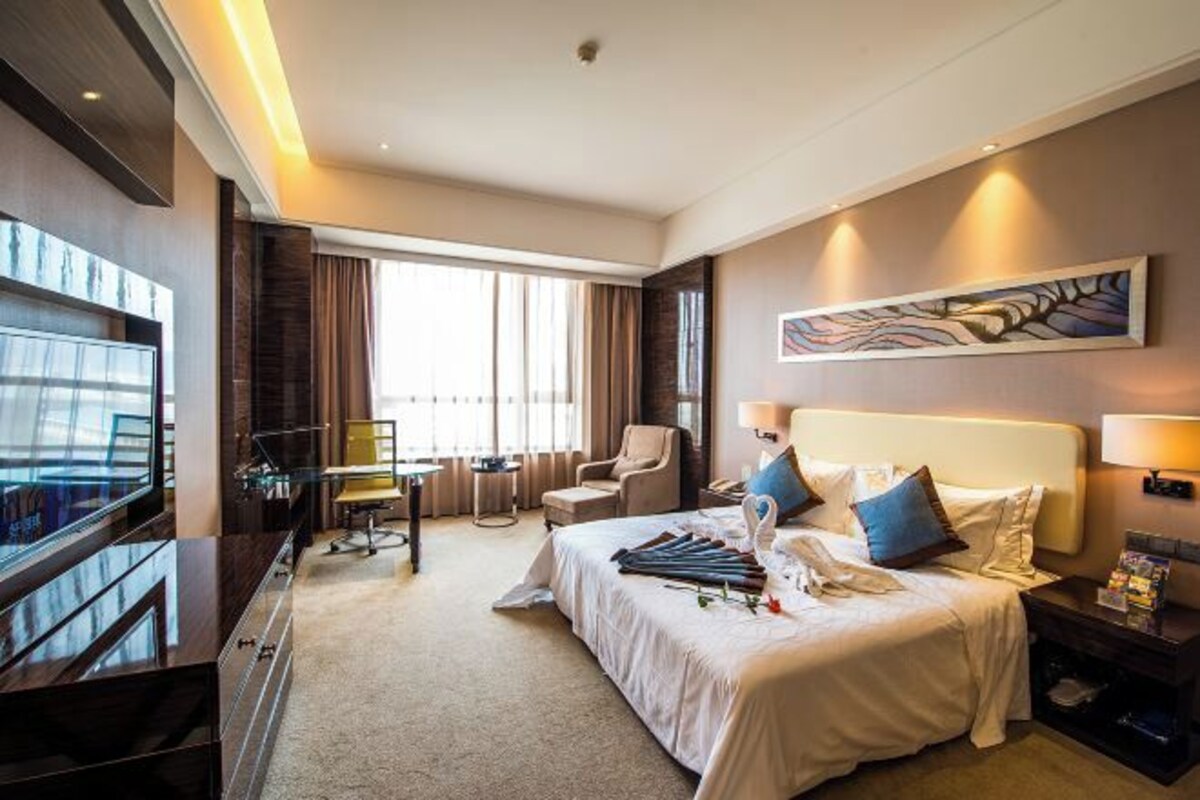 Ein Hotelzimmer mit einem großen Bett, einem Schreibtisch, einem Fernseher und einem Bild an der Wand.