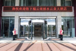 A hotel entrance with a revolving door and two attendants.