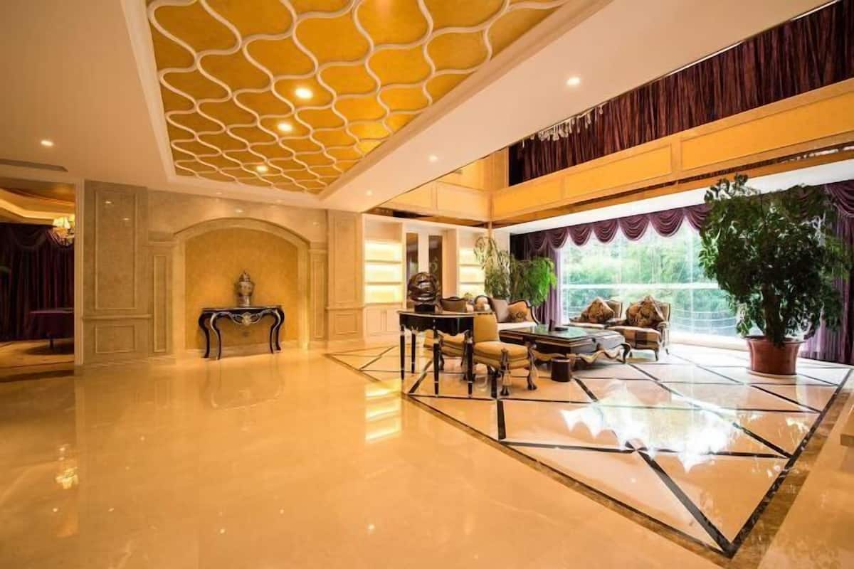 Un hall d’entrée spacieux avec un sol ciré, un coin salon avec une table et des chaises, une grande plante en pot et un plafond décoratif.
