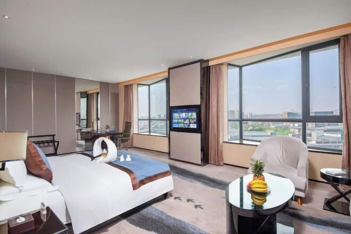 Une chambre d’hôtel avec un grand lit, un bureau équipé d’un ordinateur, une télévision et une vue sur la ville grâce à de grandes fenêtres.