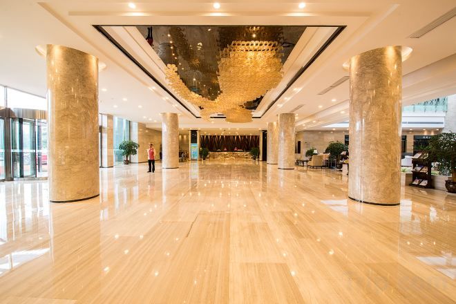 A spacious lobby with a polished floor, large columns, and a central chandelier.