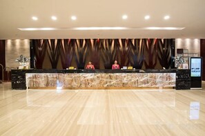 A hotel reception area with a marble counter, two receptionists, and a modern wall design.