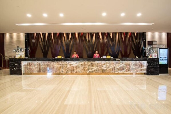 Zona de recepción de un hotel con mostrador de mármol, dos recepcionistas y un diseño de pared moderno.