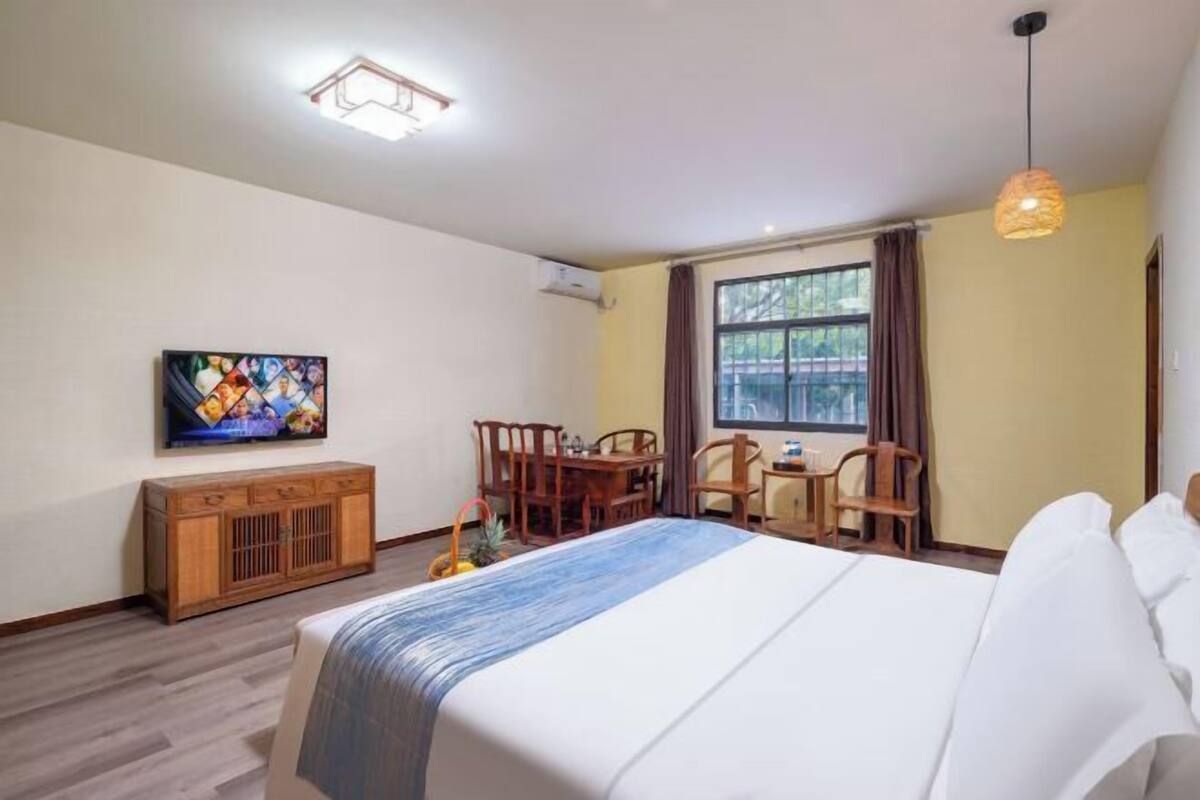 Une chambre d’hôtel comprenant un lit, une télévision, une table à manger avec des chaises et une fenêtre avec des rideaux.