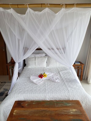 A neatly made bed with a white canopy, a wooden nightstand with a book, and a small table in front of the bed.