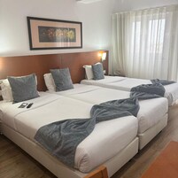 Habitación de hotel con dos camas, un cuadro floral enmarcadosobre las camas y una ventana con cortinas traslúcidas.