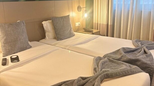 Hotelkamer met twee bedden, een wandairconditioner, een bedlampje en een raam met gordijnen.