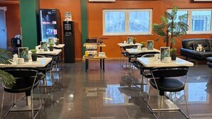 Een modern restaurant met een glanzende vloer, meerdere tafels en stoelen, en een centraal bedieningsgedeelte.
