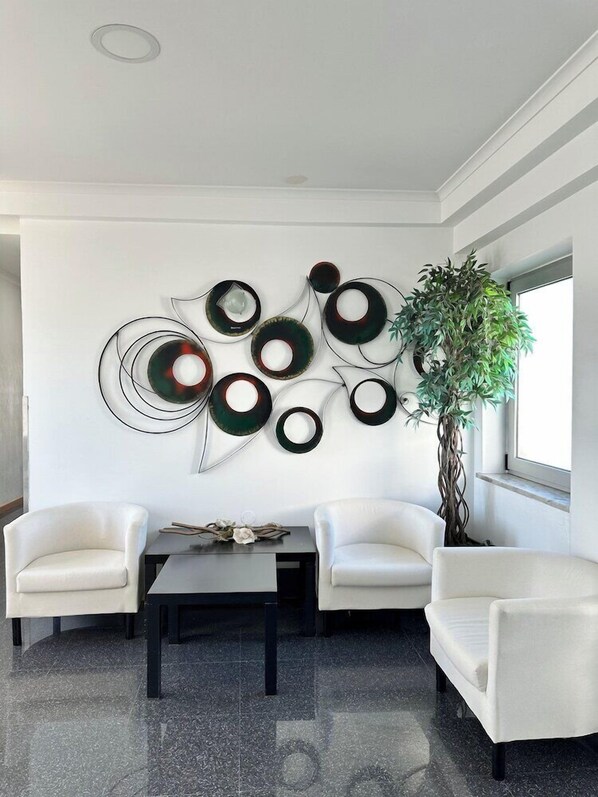 Ein modernes Wohnzimmer mit weißer Wand, einem großen abstrakten Kunstwerk, zwei wei ßen Sesseln, einem Couchtisch und einer Topfpflanze.