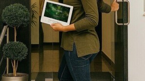 Een vrouw houdt een tablet vast voor een hotel ingang, met een bord waarop staat 