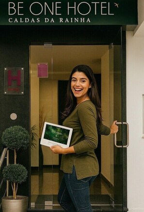 A woman holding a tablet outside a hotel entrance with a sign reading "BE ONE HOTEL CALDAS DA RAINHA".