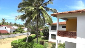 Um edifício branco com telhado de telhas vermelhas, rodeado por vegetação e palmeiras.
