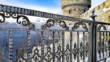 A snow-covered gate with intricate metalwork, leading to a historic stone tower.