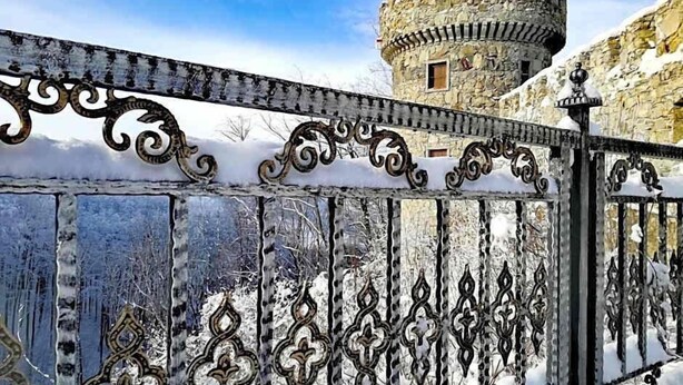 A snow-covered gate with intricate metalwork, leading to a historic stone tower.