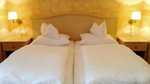 A double bed with white linens and pillows, flanked by two bedside tables with lamps, in a room with textured walls.