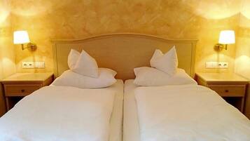 A double bed with white linens and pillows, flanked by two bedside tables with lamps, in a room with textured walls.