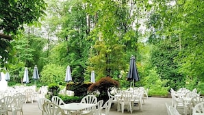 An outdoor patio area with white plastic chairs and tables, surrounded by lush greenery and trees. - Grünes Türl (Bad Schallerbach)