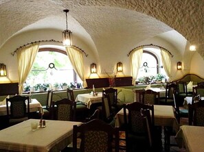 An interior with tables and chairs, arched ceilings, and windows with curtains.