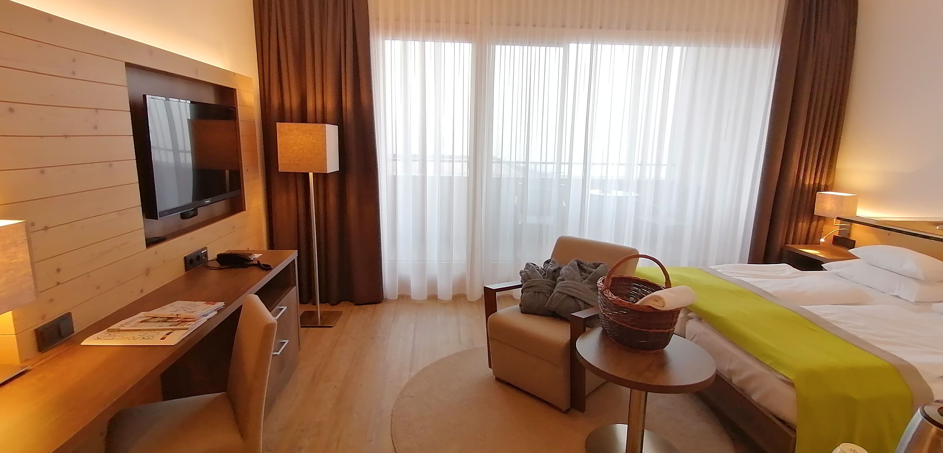 Habitació d'hotel amb un llit, un escriptori, una cadira, una televisió i una finestra amb cortines.