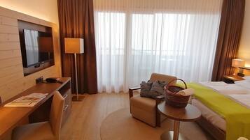 Habitació d'hotel amb un llit, un escriptori, una cadira, una televisió i una finestra amb cortines.