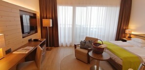 Et hotelværelse med seng, skrivebord, stol, fjernsyn og et vindue med gardiner.