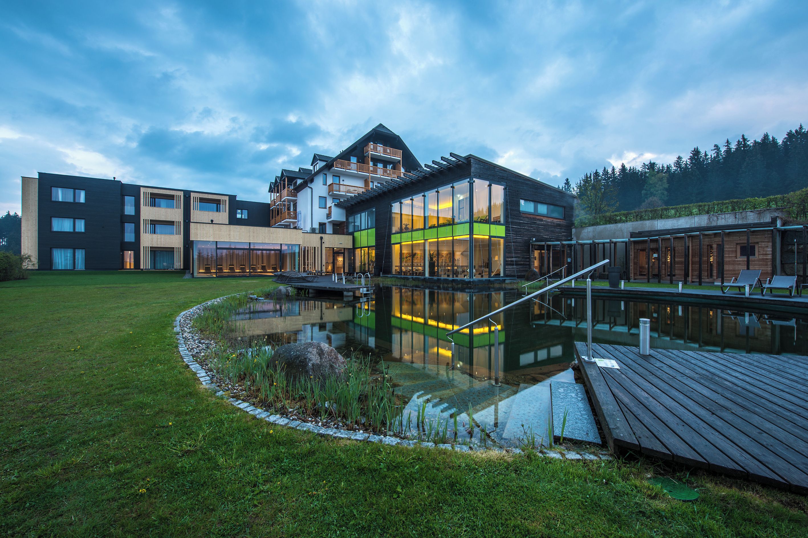 A modern building with a glass facade, a wooden deck, and a small pond.