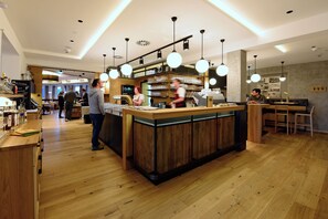 Interior de una cafetería con mostrador de madera, lámparas colgantes y una máquina de espresso a la vista.