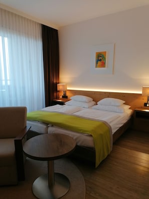 Una habitación de hotel con una cama, una silla, una mesita y un cuadro en la pared.