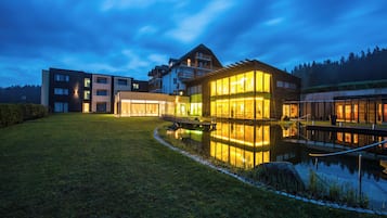 Un edificio moderno con un estanque reflectante, rodeado de césped cuidado y un cielo despejado.