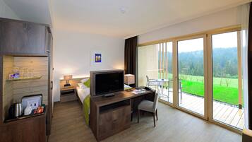 Habitación de hotel con cama, escritorio, silla, televisor y un ventanal con vistas a un paisaje verde.