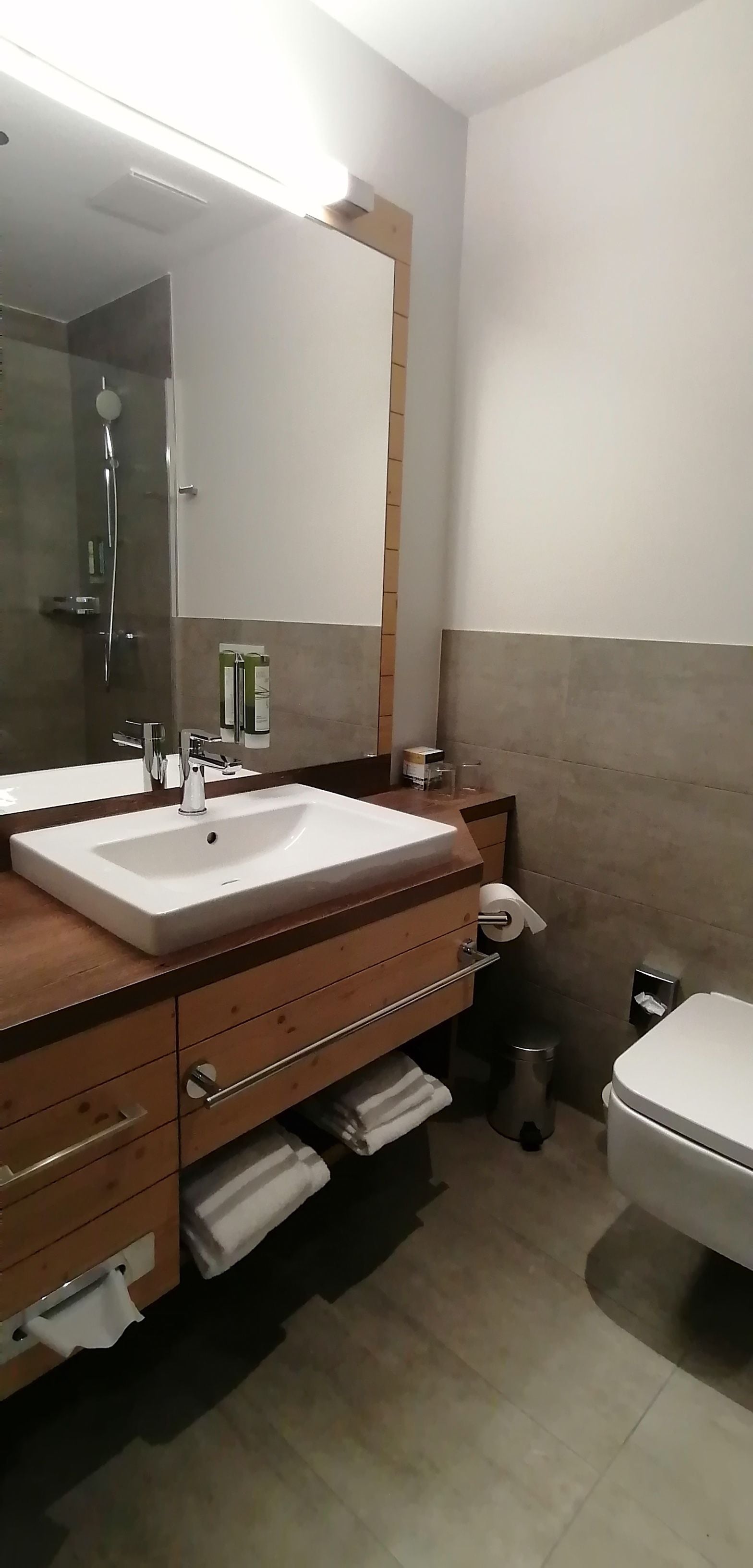 A modern bathroom with a large mirror, a sink, a toilet, and a shower.