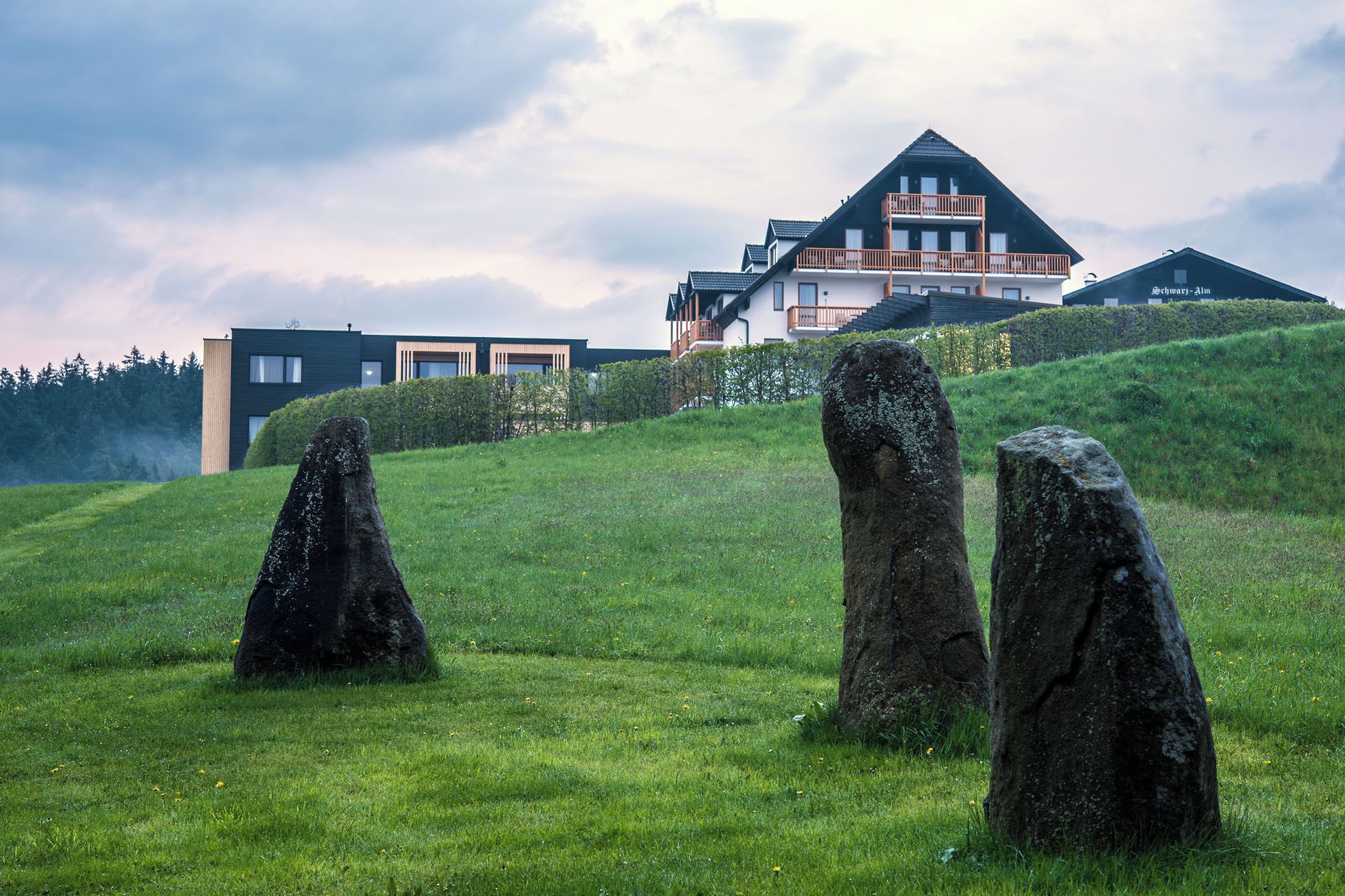 A modern building with a balcony and a grassy hill with three large rocks.