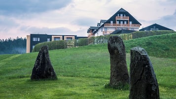 A modern building with a balcony and a grassy hill with three large rocks.
