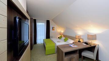 Habitación de hotel con cama, escritorio, silla, televisor y ventana con cortinas.