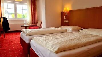 Ein Hotelzimmer mit zwei Betten, einem kleinen Tisch mit Stuhl, einer Lampe und einem Fenster mit Vorhängen.