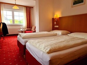 Une chambre d’hôtel avec deux lits, une petite table avec une chaise, une lampe et une fenêtre avec des rideaux.