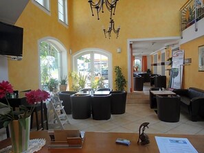 Un hall d’hôtel avec un plafond haut, un lustre, un comptoir d’accueil et une vue sur l’extérieur.