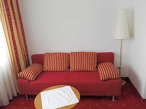A red sofa with striped cushions, a white table, and a floor lamp in a room with patterned carpet.
