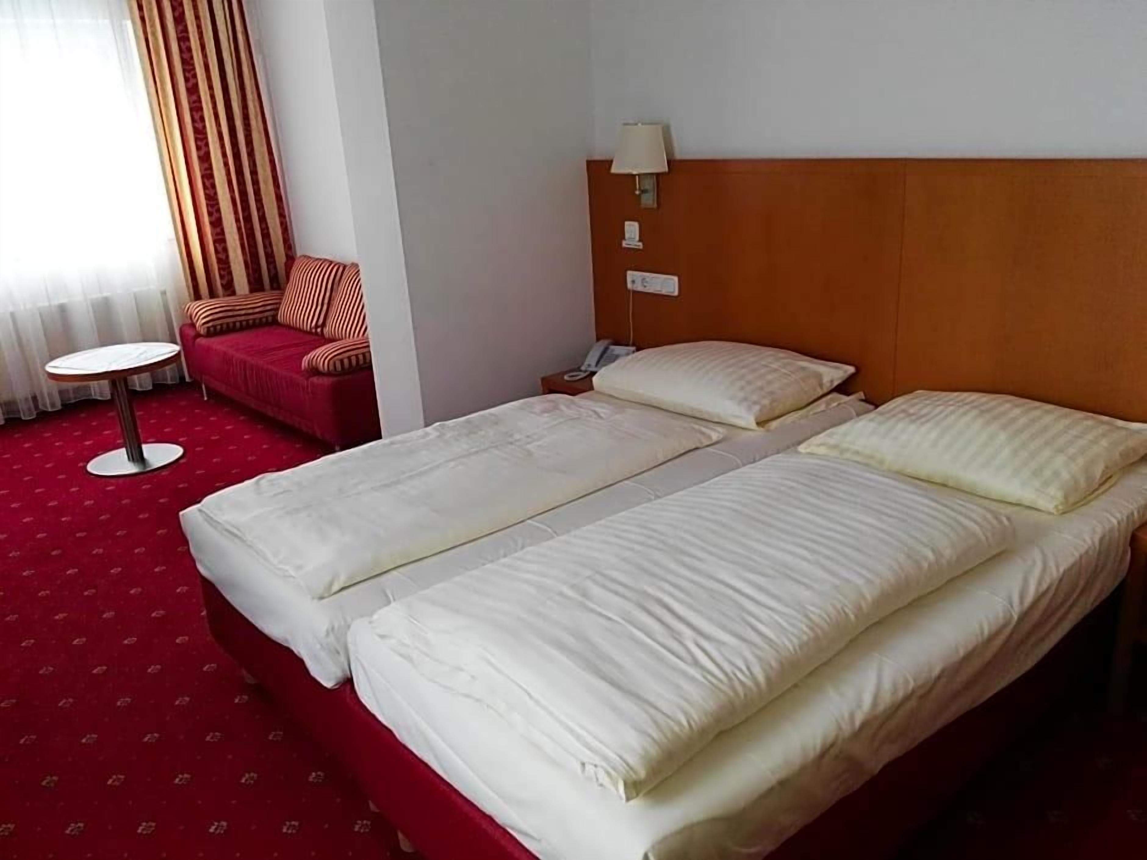 Een hotelkamer met twee bedden, een rode bank, een kleine ronde tafel en een lamp.