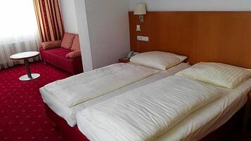 Een hotelkamer met twee bedden, een rode bank, een kleine ronde tafel en een lamp.