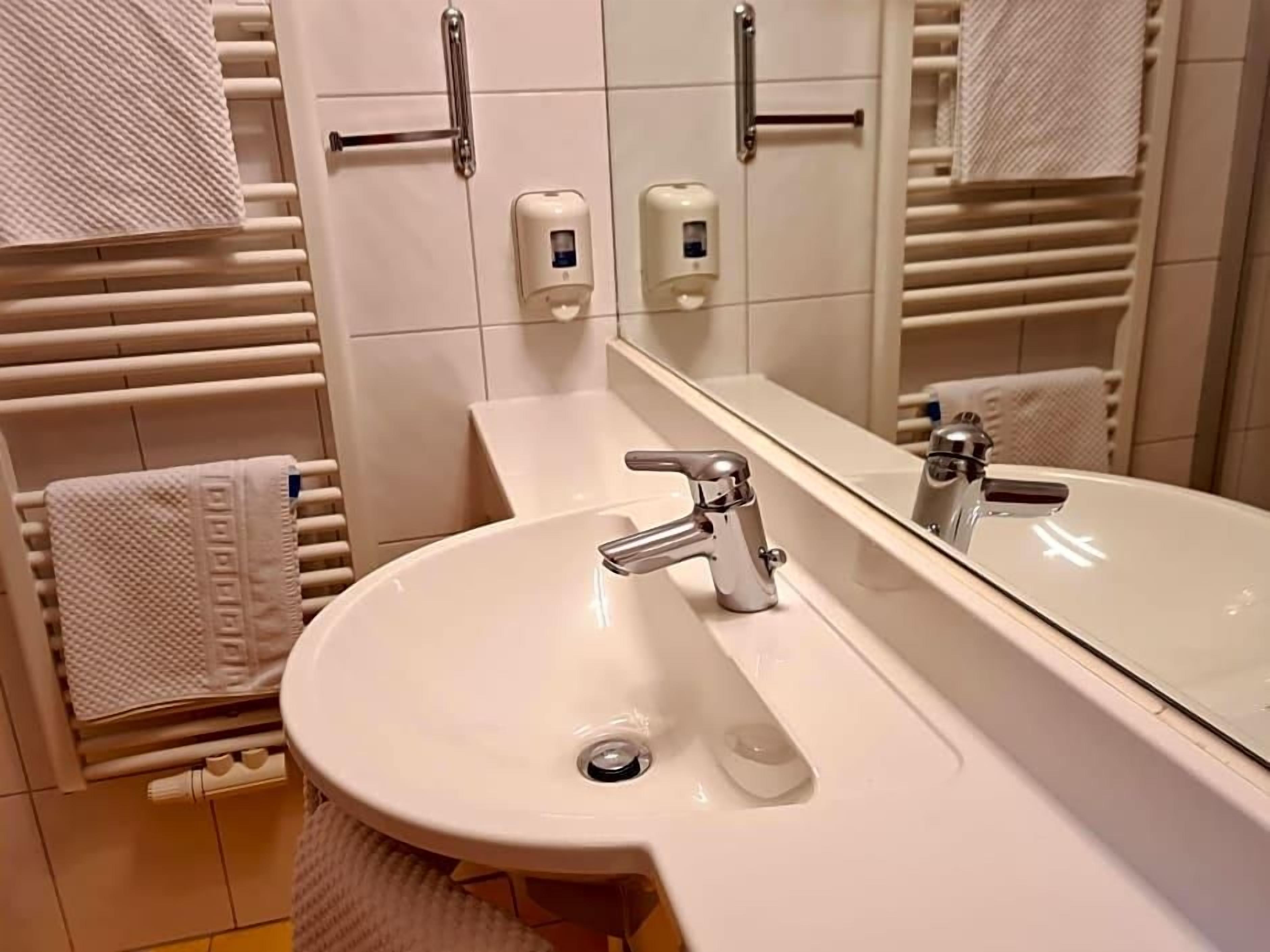 A bathroom with a white sink, a mirror, and towel racks.